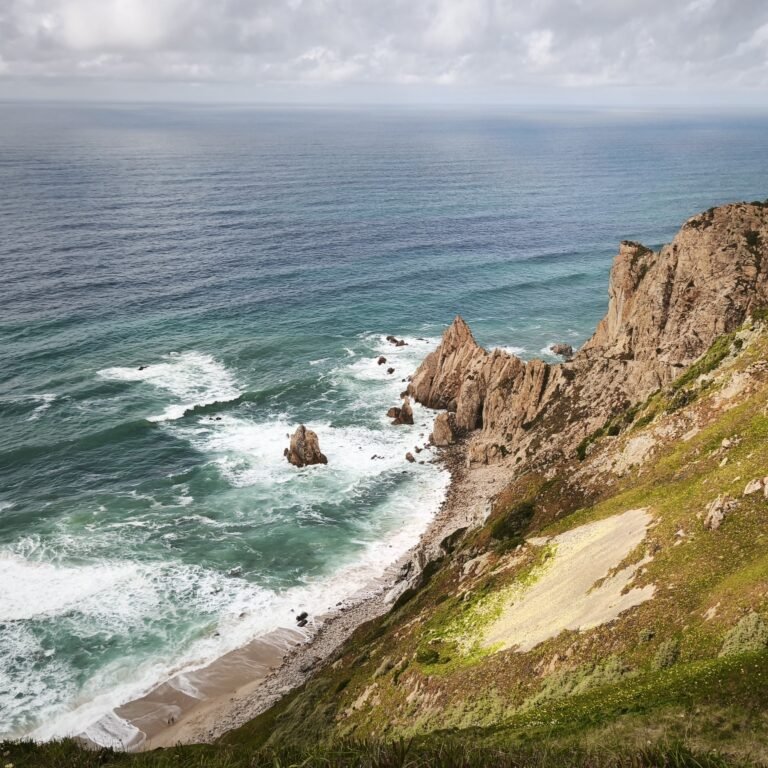 Wide shot of a secluded sandy beach nestled between towering cliffs in Cascais.