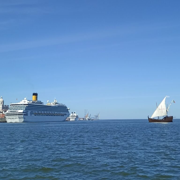 Sailboat on the Tagus River with a large cruise ship and Lisbon's skyline in the distance.