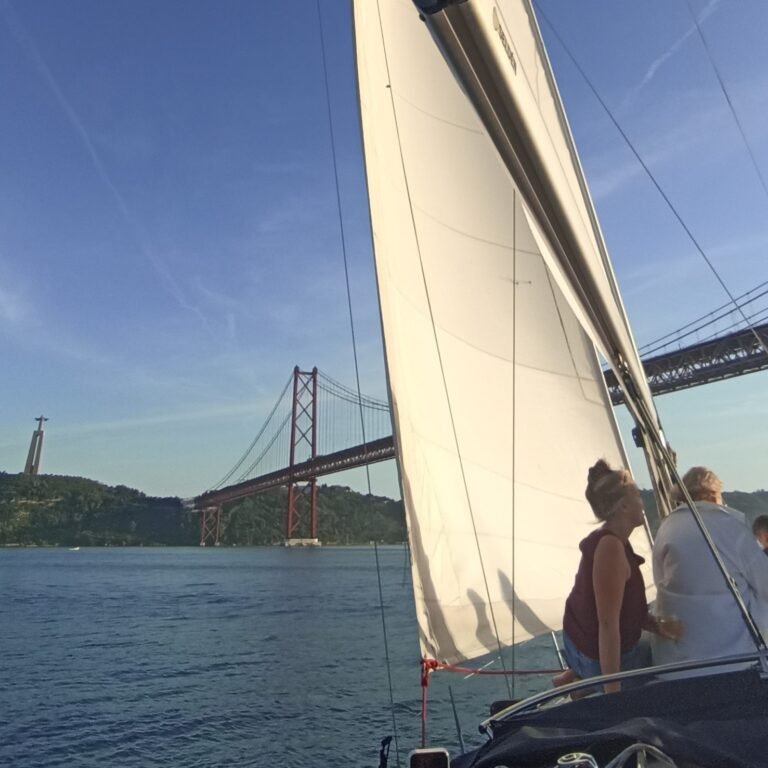 People on a sailboat deck enjoying views of Lisbon from the Tagus River.