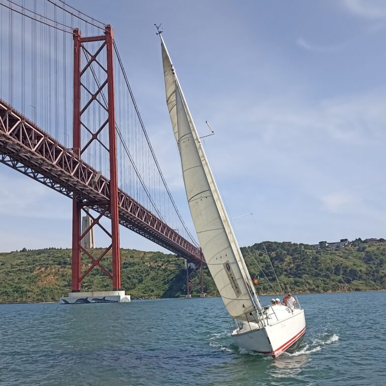 Sailboat's white sail against a bright blue sky, catching the wind in Lisbon.