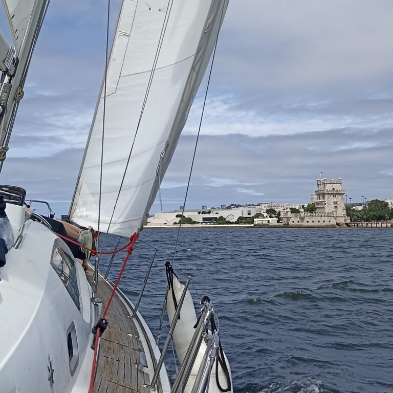 View from a sailboat deck towards the front, showing ropes and open water in Lisbon.