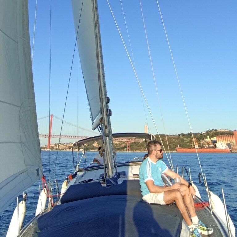 Person on a sailboat deck, enjoying the sunny weather and river views in Lisbon.