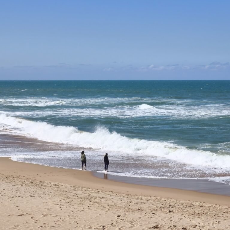 Wide sandy beach with people enjoying the shore and distant cliffs in Cascais.