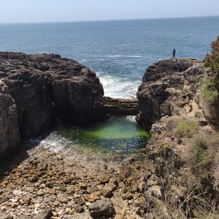 Rocky cliff overlooking the deep blue ocean with seagulls flying in Cascais.