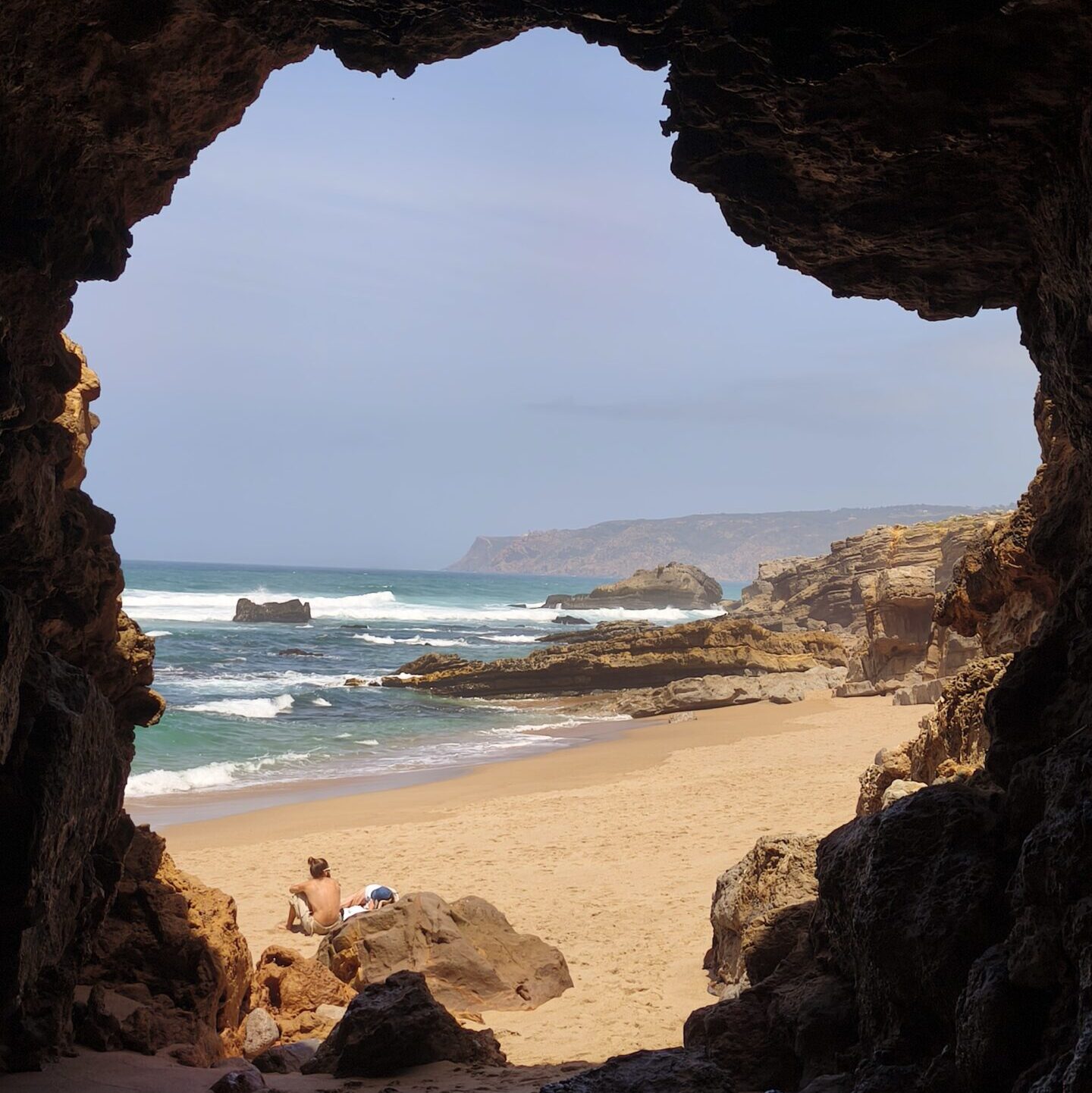 Panoramic view of a secret beach in Cascais framed by a natural rock cave opening.