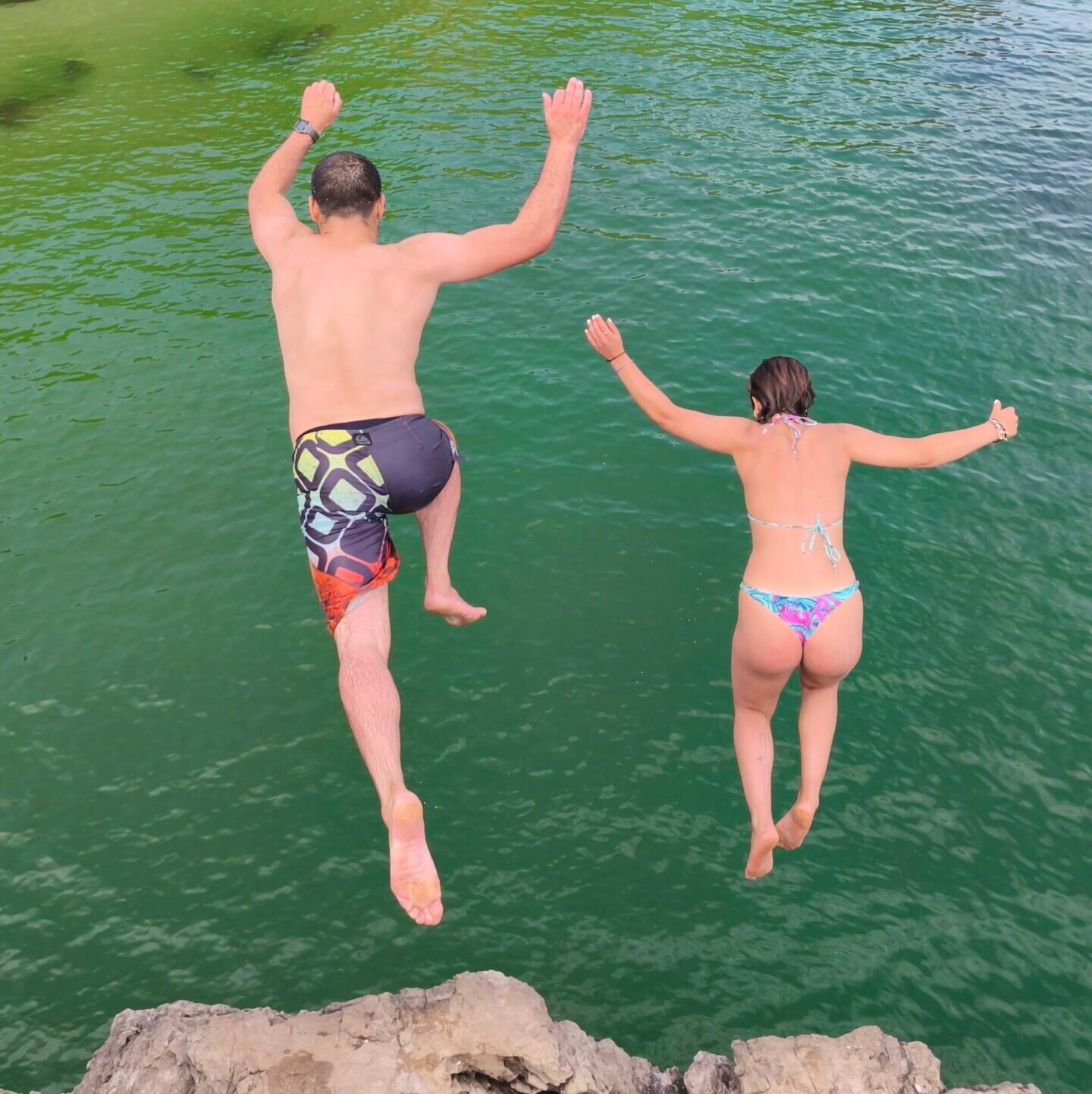 Two people jumping off a high cliff into the clear ocean during a private cliff jumping tour in Cascais.