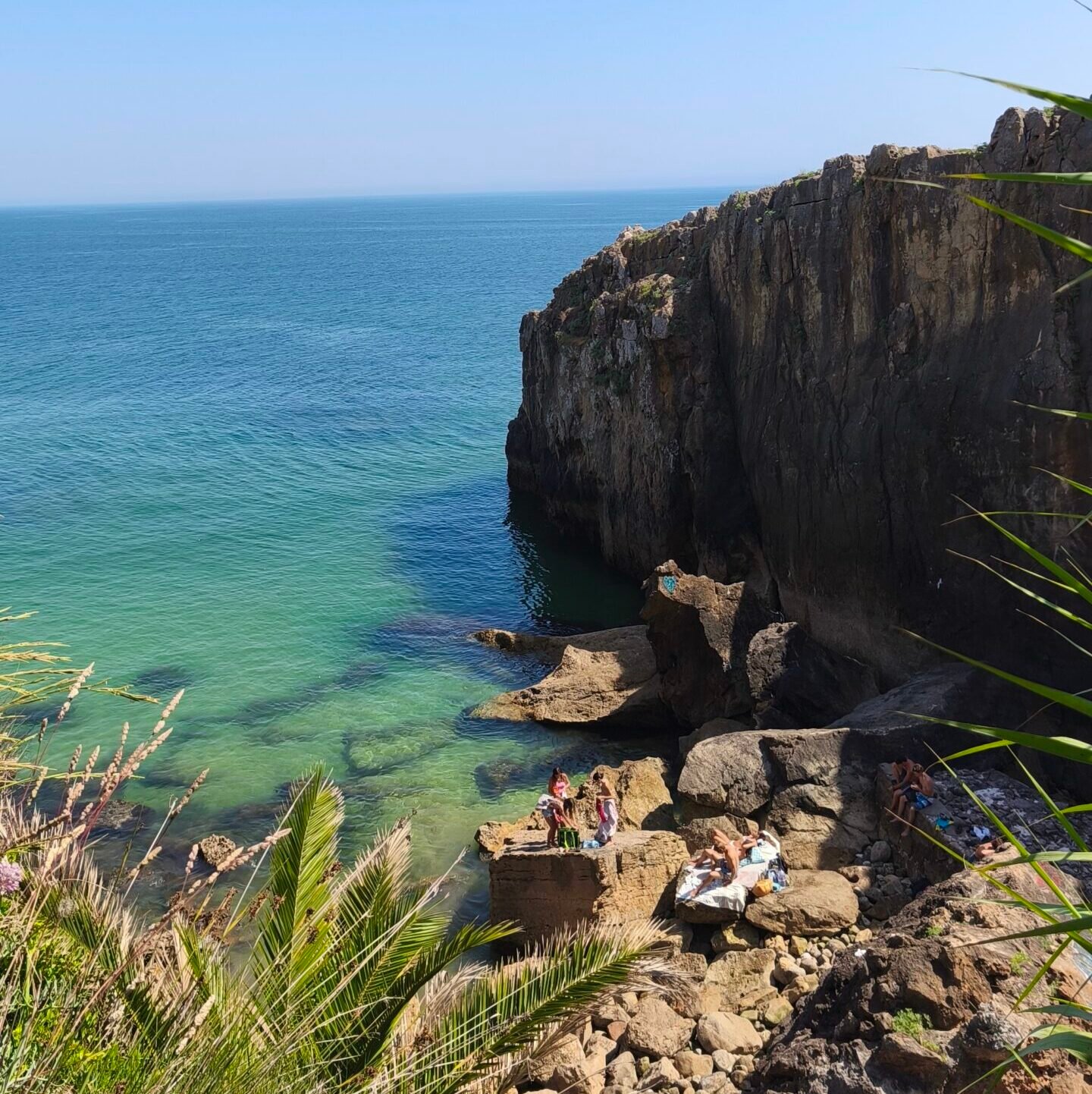 Crystal-clear green waters inside a hidden natural swimming pool surrounded by rocks in Cascais.