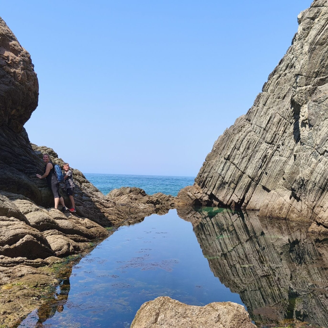 Narrow path between massive rock formations leading to a secluded natural pool in Cascais.