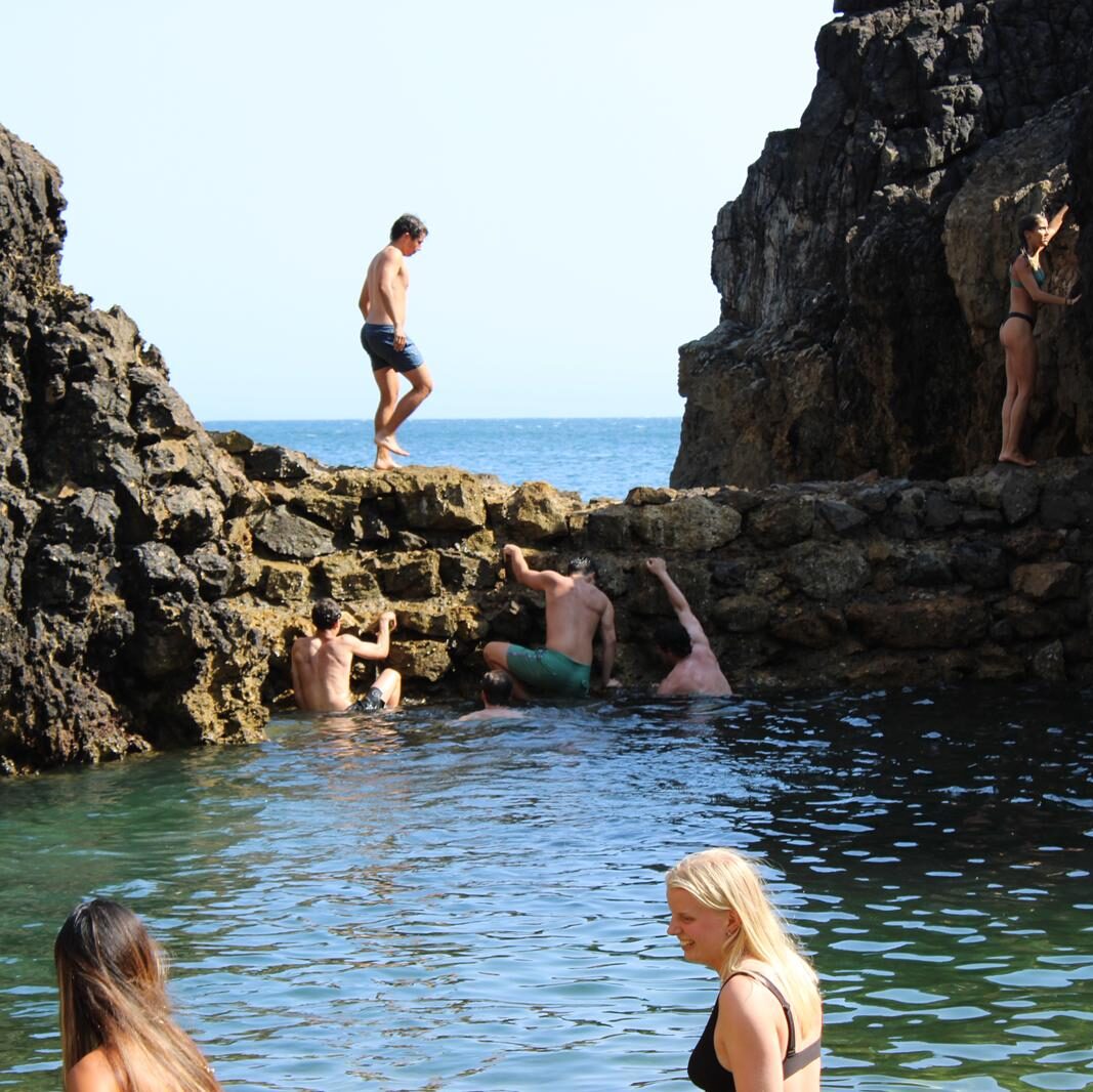 Tour guests swimming and floating in a deep natural rock pool surrounded by high cliffs in Cascais.