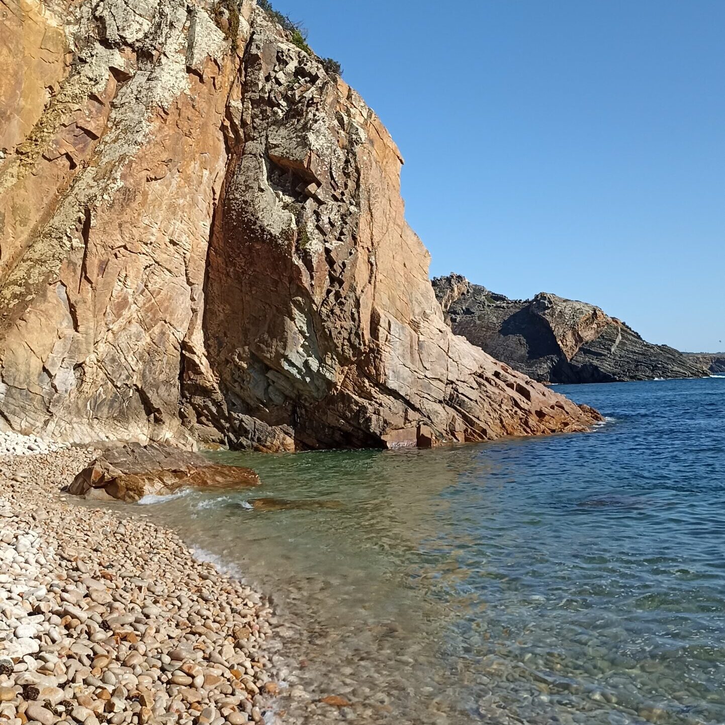 Shallow transparent sea water washing over golden coastal rocks during a private tour in Cascais.