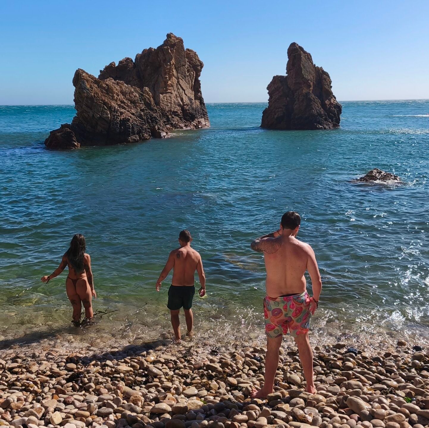 Tour participants walking by the shore next to giant sea rocks on a sunny day in Cascais.