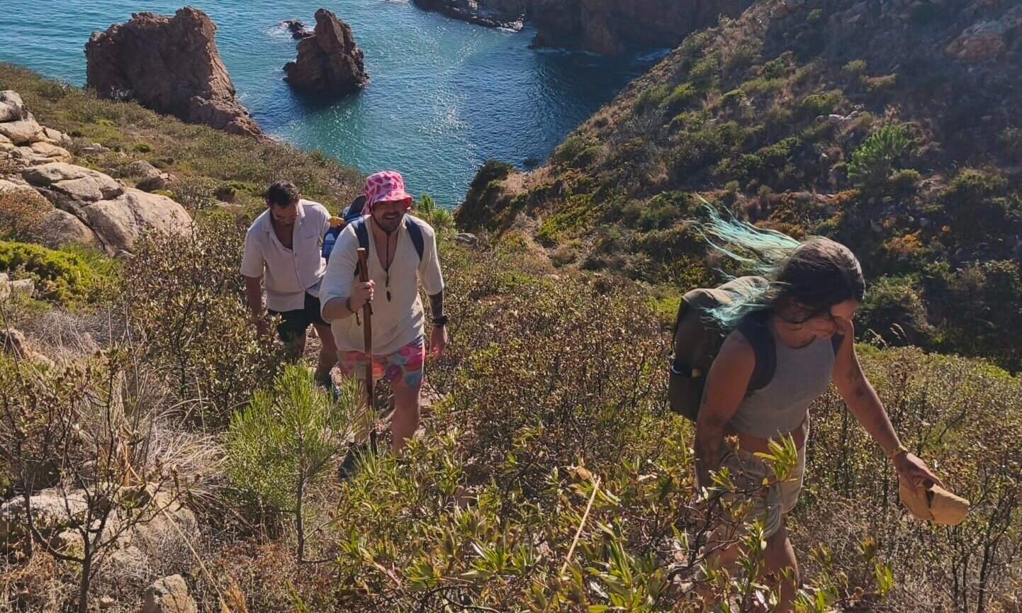 Hikers walking up a trail surrounded by wild coastal vegetation with ocean views in Cascais.