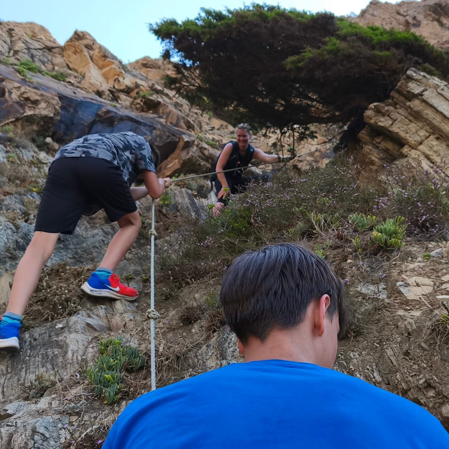 An adventurous tourist carefully climbing a steep dirt slope on the cliffs of Cascais.